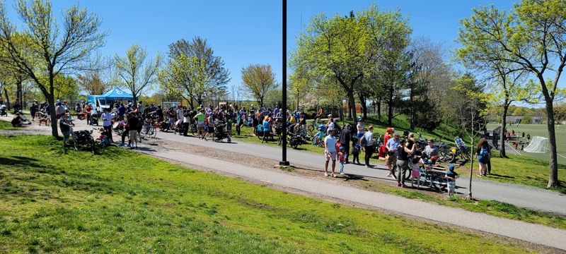 A large crowd of people gather along in a park, surrounding a large number of cargo bikes.